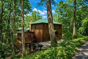 A cabin with a green roof, surrounded by trees, and a wooden deck.