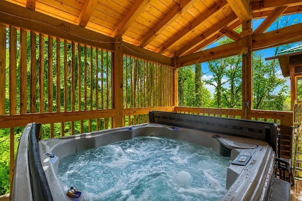 A hot tub under a wooden pergola with a view of greenery.