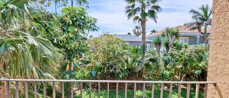 A balcony with a metal railing overlooking a garden with various plants and a house in the background.