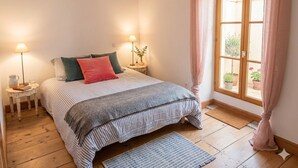 Een slaapkamer met een bed, twee bedlampen, een raam met gordijnen en uitzicht op de omgeving.
