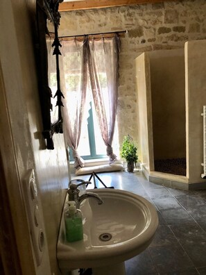 A bathroom with a sink, a window with curtains, a plant, and a stone wall.