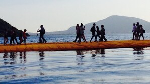 A group of people walking along a beach with a body of water and a mountain in the background.
