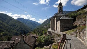 Une église en pierre dotée d’un clocher, entourée de maisons à étages et de montagnes verdoyantes.