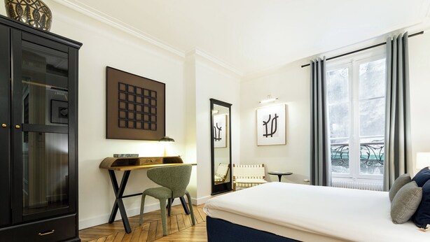 Habitación de hotel con cama, escritorio, silla, armario y ventana grande.