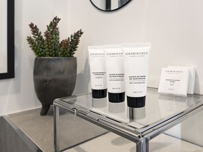 Une table en verre sur laquelle sont posées trois bouteilles de gel douche Gemology et une boîte de savon.