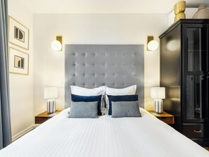 A hotel room with a large bed, two bedside lamps, a dark wooden wardrobe, and framed pictures on the wall.