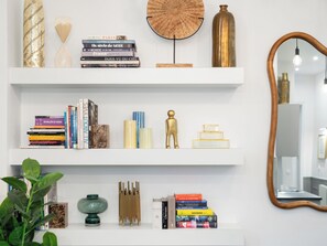 Una estantería blanca con libros, objetos decorativos y un espejo.