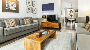 Uma sala de estar moderna com um sofá cinzento, mesa de centro de madeira e uma televisão de tela plana.