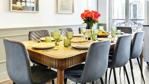 Mesa de jantar posta com pratos, copos e um vaso de flores, rodeada por cadeiras.