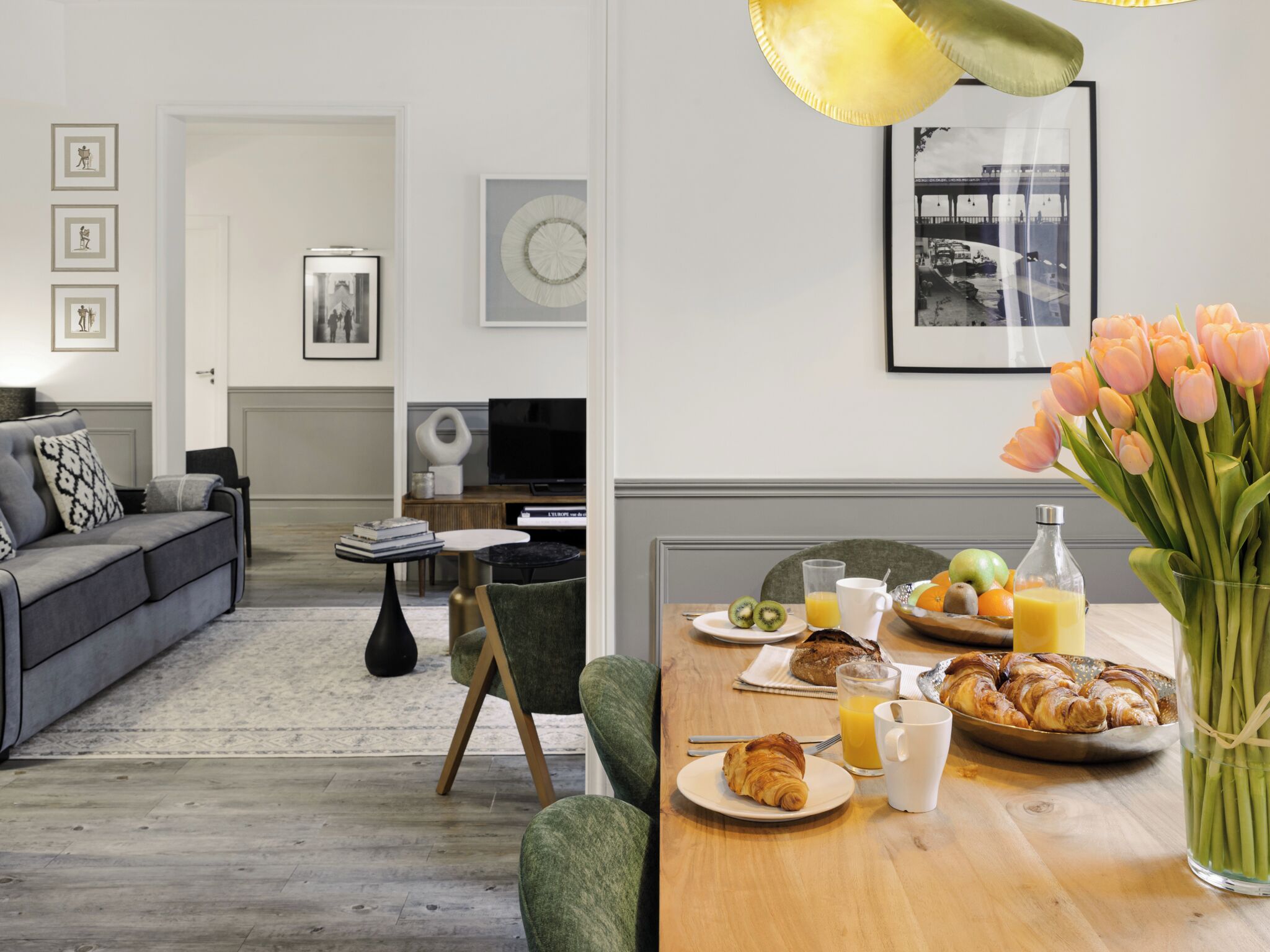 Un soggiorno moderno con un divano grigio, un tavolino da caffè e un'area pranzo con prodotti per la colazione.