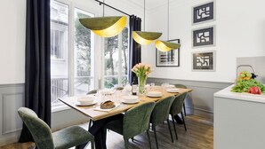 A dining area with a wooden table set for six, green upholstered chairs, and pendant lighting. - LivinParis | Luxury AC 4 Bedrooms Opera I (Paris)