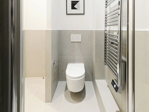 A modern bathroom with a toilet, a towel rack, and a wall-mounted control panel.