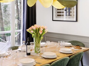 A dining table set with plates, glasses, and a bottle of wine, with a vase of flowers and a framed picture on the wall.