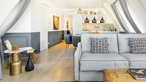 A modern loft apartment with a dining area, kitchen, and a grey sofa with patterned cushions. - LivinParis | Luxury AC 3 Bedrooms Le Louvre - Eiffel View (Paris)