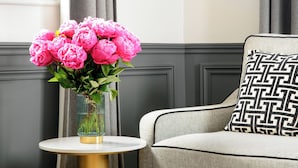 A room with a round table, a vase with flowers, a chair with a patterned cushion, and a wall with paneling. - LivinParis | Luxury AC 3 Bedrooms Le Louvre - Eiffel View (Paris)
