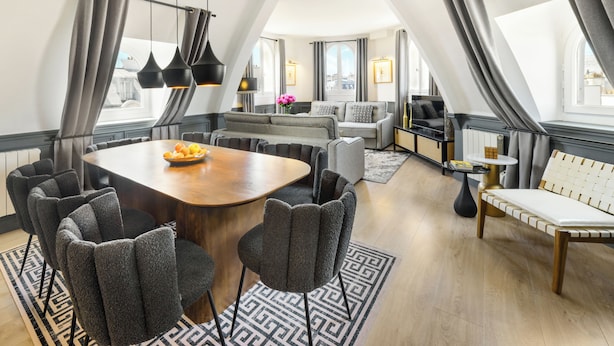 A modern living room with a dining area, grey upholstered furniture, a wooden dining table, and a black and white patterned rug. - LivinParis | Luxury AC 3 Bedrooms Le Louvre - Eiffel View (Paris)