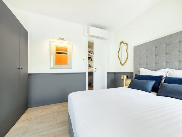 Une chambre moderne avec un grand lit, une armoire, une table de chevet avec une lampe et un miroir fixé au mur.