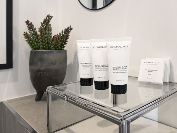 A bathroom with a glass table displaying three bottles of Gemology cosmetics and a small box of soap.