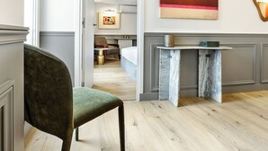 Hotellihuoneessa on vihreäverhoiltu nojatuoli, marmorinen sivupöytä, sänky, taulu ja seinällä oleva peili.