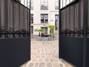 A courtyard with a stone floor, black metal gates, and potted plants. - LivinParis | Luxury AC 4 Bedrooms Le Louvre I (Paris)