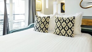 Hotellihuone, jossa on sänky, lamppu, ikkuna, jossa on verhot, ja taulu seinällä.