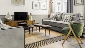 A modern living room with a grey sofa, a coffee table, a TV on a wooden stand, and a patterned rug.