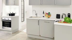 A compact kitchen with a built-in oven, a sink, and a countertop with a cutting board, vegetables, and a bottle.