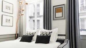 A neatly arranged hotel room with a large bed, a side table, and a view of the city through the window.