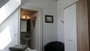 A bedroom with a bed, a black chair, a wooden wardrobe, a white sink, and a framed picture on the wall. - Small vacation apartment at Wulfkamp (Velen)