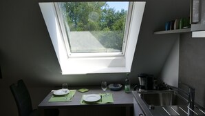 A dining area with a table set for two, a window with a view of greenery, and a kitchen area with a sink and cabinets. - Small vacation apartment at Wulfkamp (Velen)