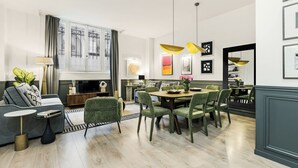 A modern living room with a sofa, coffee table, and TV, a dining area with a table and chairs, and a large window with curtains. - LivinParis | Luxury AC 3 Bedrooms République I (Paris)