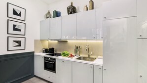 A modern kitchen with white cabinets, a built-in oven, a sink, and a coffee maker. There are three framed pictures on the wall above the counter. - LivinParis | Luxury AC 3 Bedrooms République I (Paris)