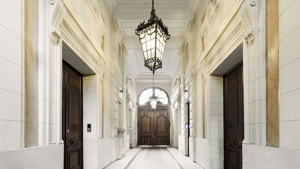 A long, narrow hallway with white walls and marble floors, leading to a large wooden door at the end. - LivinParis | Luxury AC 3 Bedrooms République I (Paris)