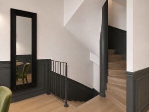Un escalier avec une rampe noire, un plancher en bois et un coin repas comprenant une table ronde et des chaises.