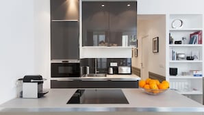 Een moderne keuken met een centraal eiland, inbouwapparatuur en een witte open plankenwand met boeken en decoratieve objecten.