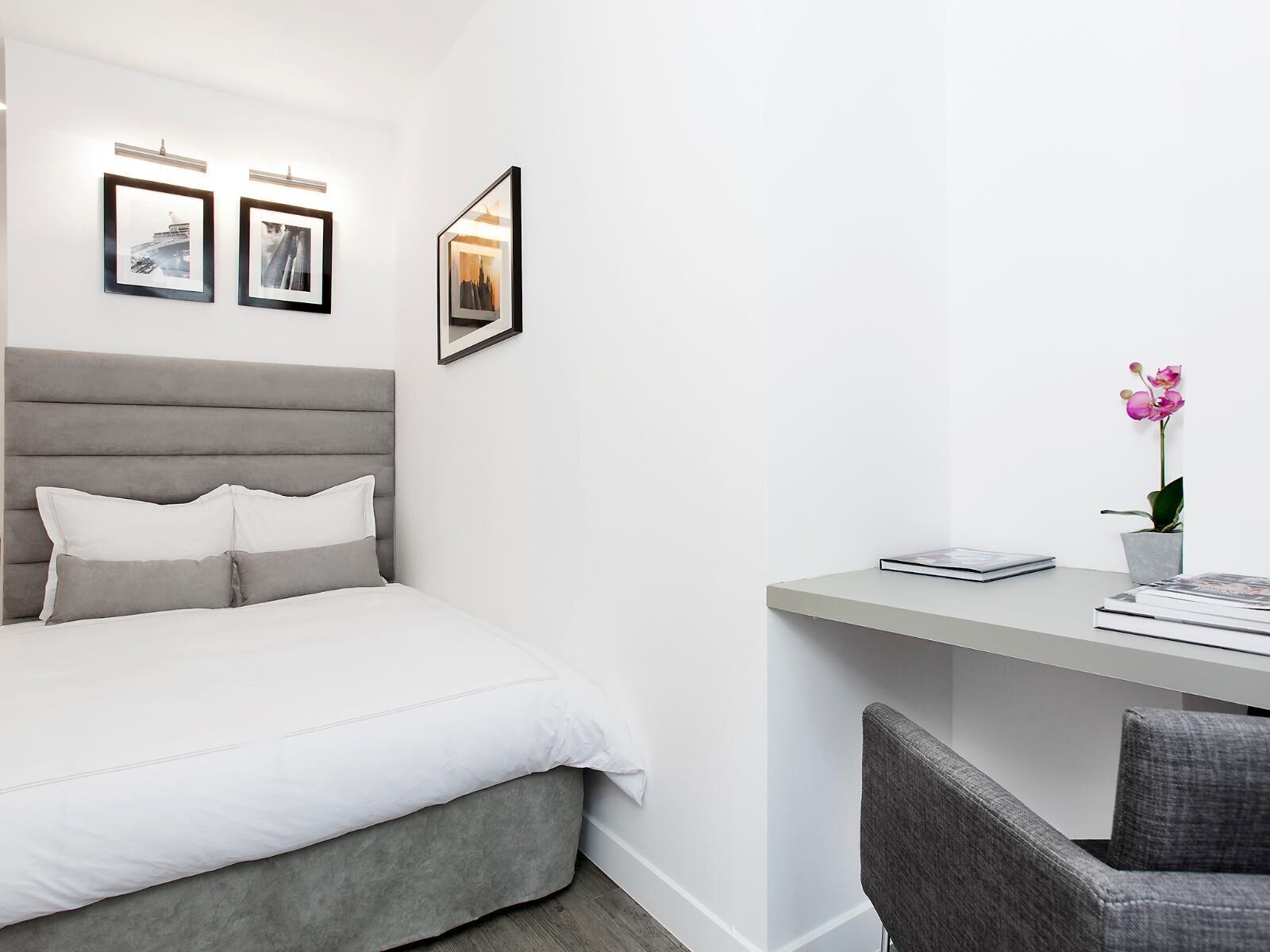 Una camera da letto moderna con un letto, una scrivania e una sedia. Alle pareti ci sono quadri incorniciati e sulla scrivania un vaso con una pianta.