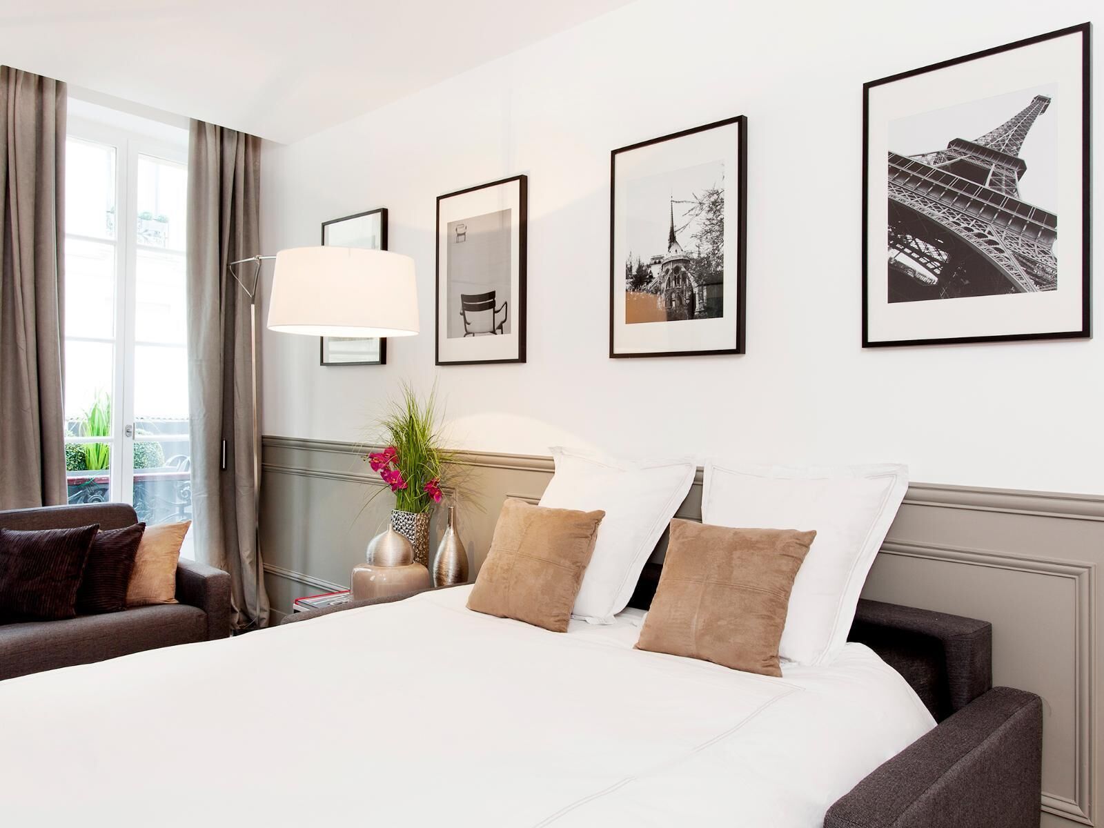 Una habitación de hotel con una cama grande, una mesita de noche con lámpara, una silla y cuadros en la pared.