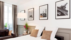 Ein Hotelzimmer mit einem großen Bett, einem Nachttisch mit Lampe, einem Sessel und gerahmten Bildern an der Wand.