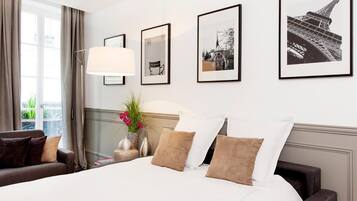 Una habitación de hotel con una cama grande, una mesita de noche con lámpara, una silla y cuadros en la pared.