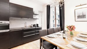 Una cocina moderna con armarios oscuros, horno empotrado y comedor con una mesa de madera preparada para cuatro.