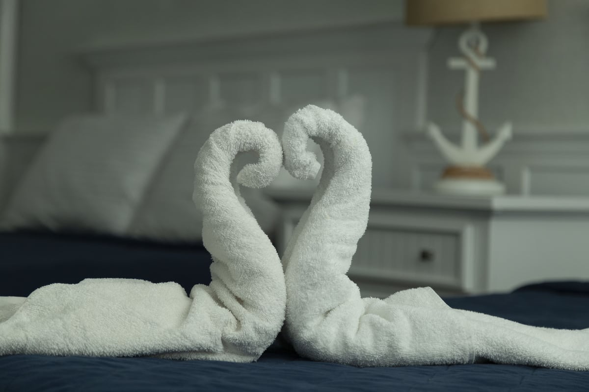 Ein Bett mit blauer Bettdecke und einem weißen Handtuch, das zu einem Herz geformt ist.