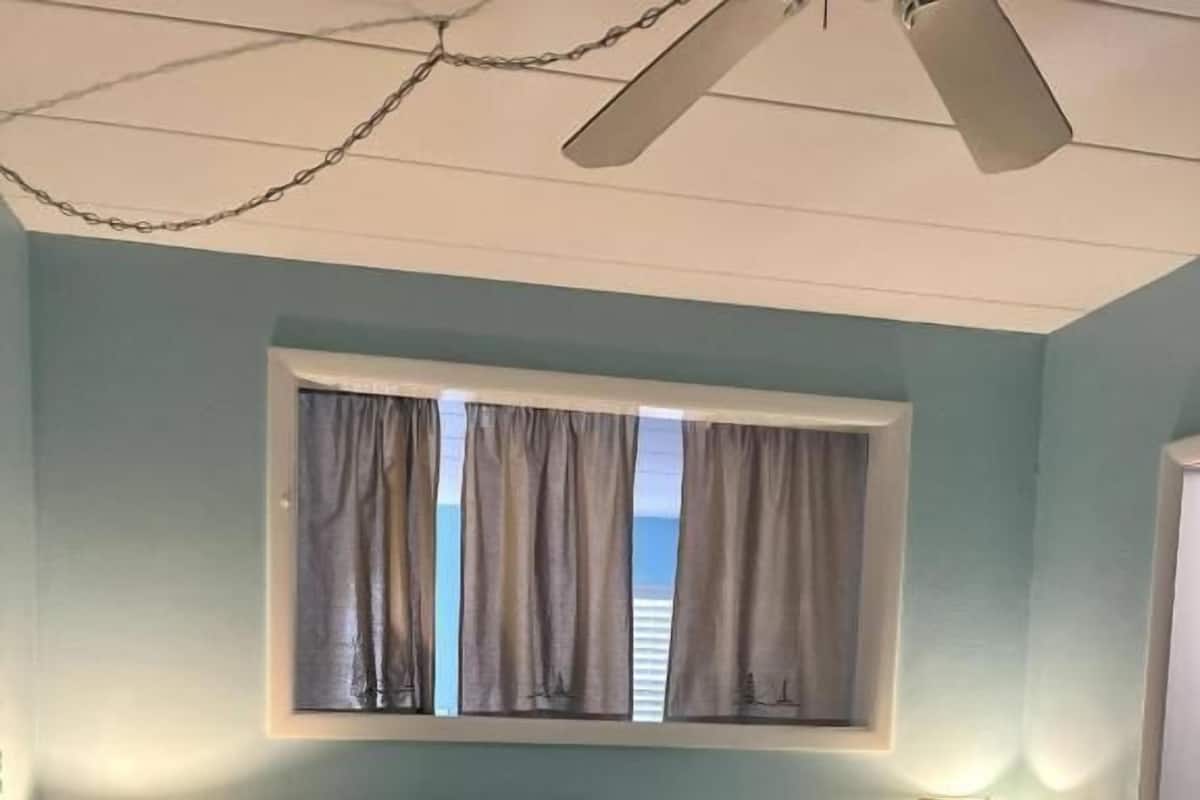 Ein Schlafzimmer mit einem Bett, zwei Nachttischlampen, einem Fenster mit Vorhängen und einem Deckenventilator.