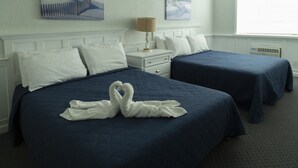 A hotel room with two beds, a nightstand, a lamp, and artwork on the walls. - Saratoga Resort (Wildwood Crest)