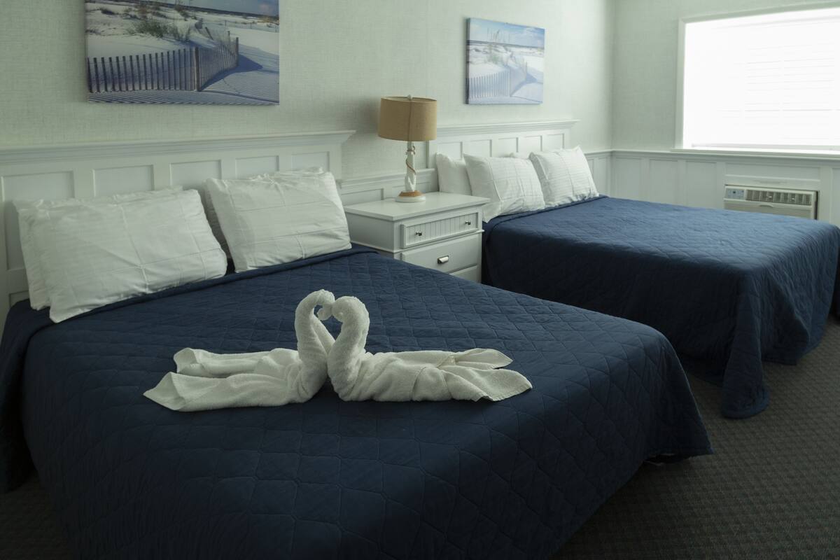Ein Hotelzimmer mit zwei Betten, einem Nachttisch, einer Lampe und Bildern an den Wänden.