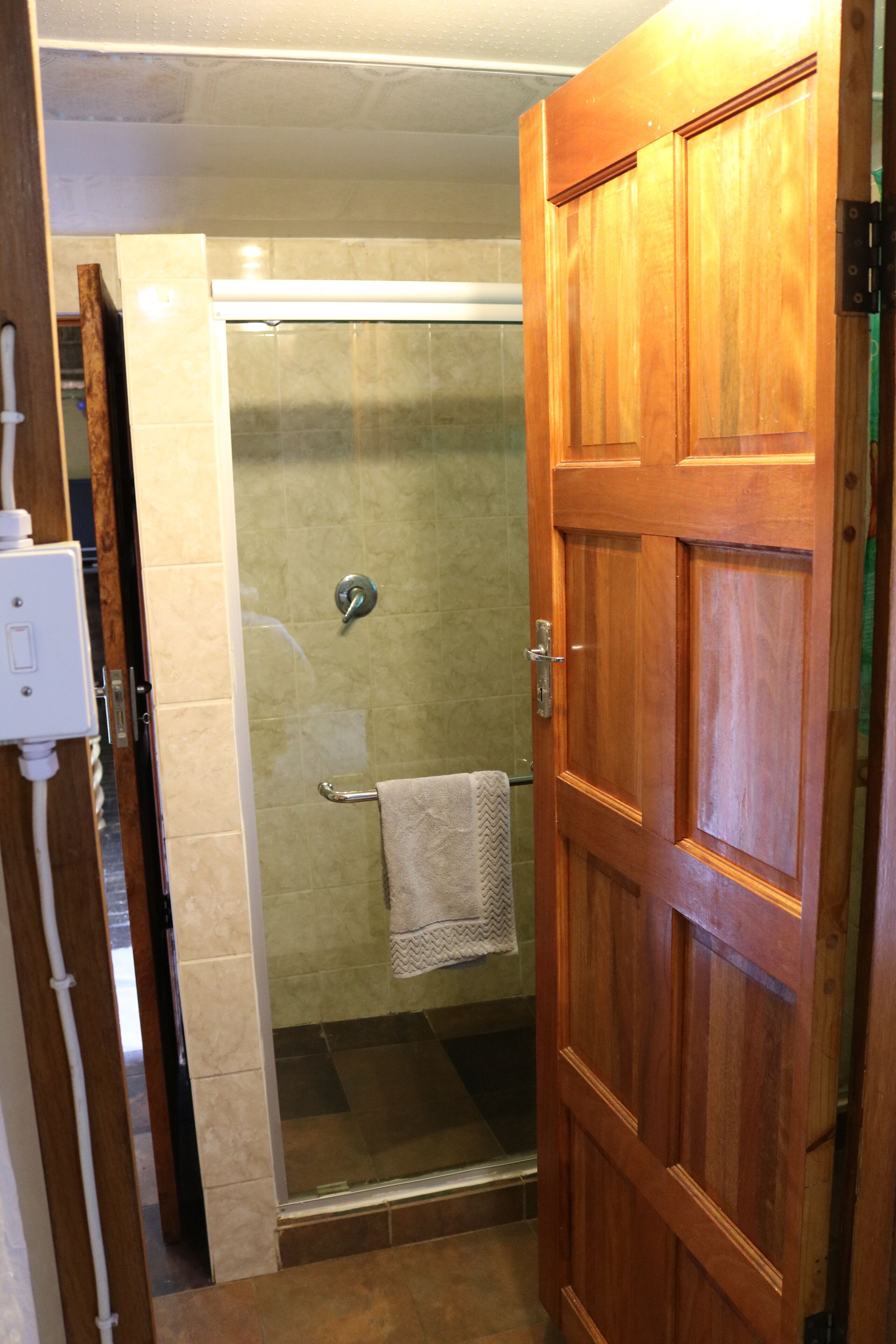 A wooden door leading to a shower area with a glass door and a towel hanging on the wall.