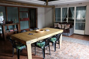 Uma sala de jantar com mesa e cadeiras de madeira, uma estante e um sofá com almofadas estampadas.