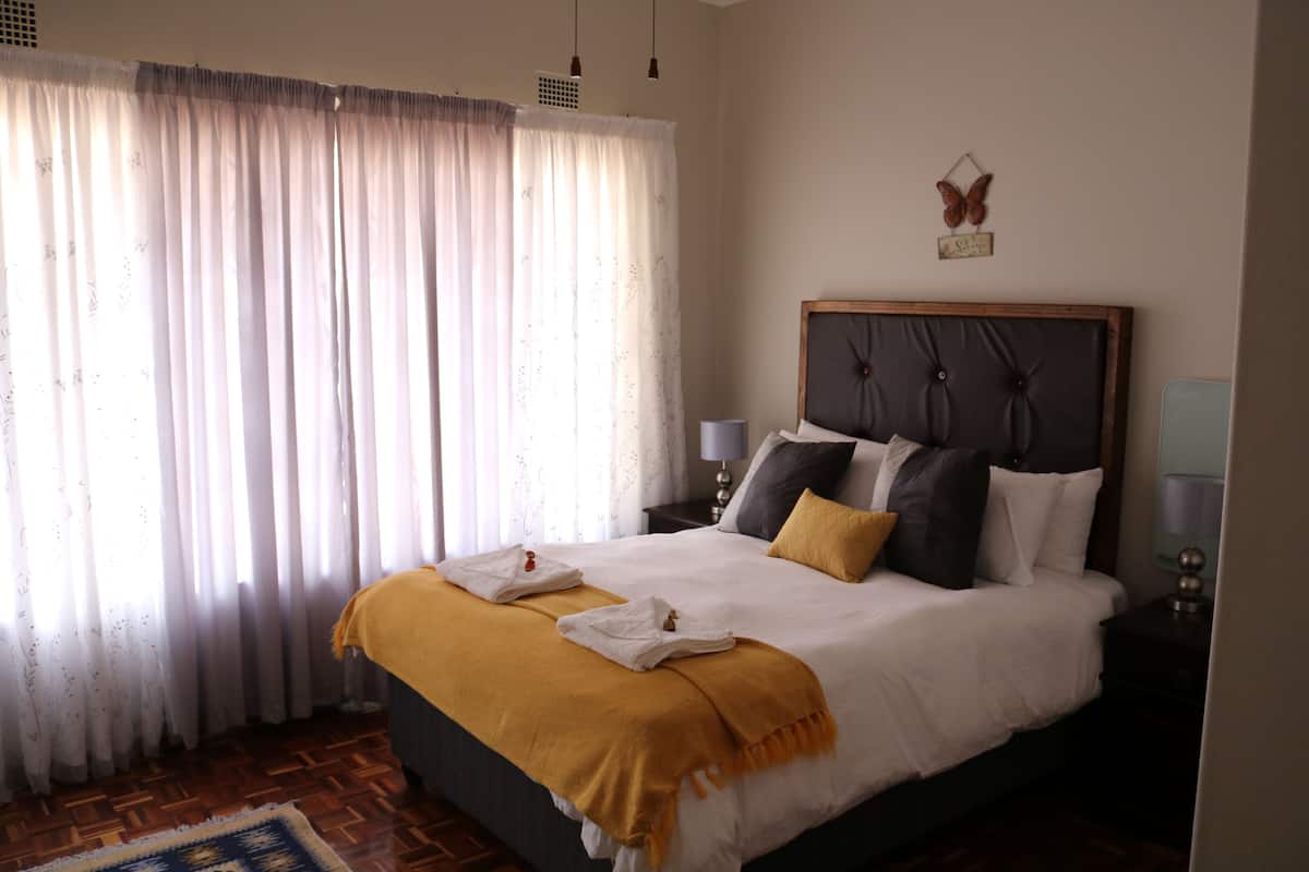 A neatly made bed with a headboard, a bedside table with a lamp, and a window with curtains.