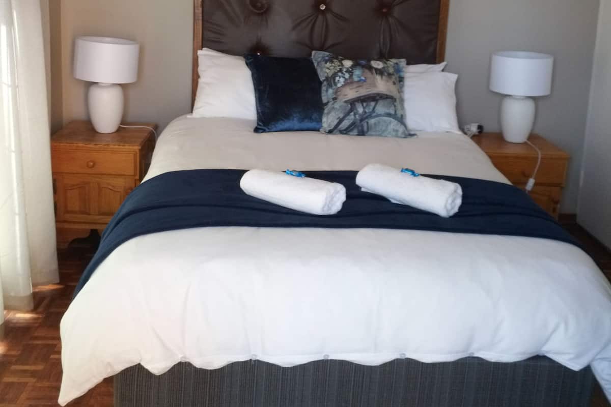 A neatly made bed with a headboard, two bedside lamps, and a wall-mounted air conditioner.
