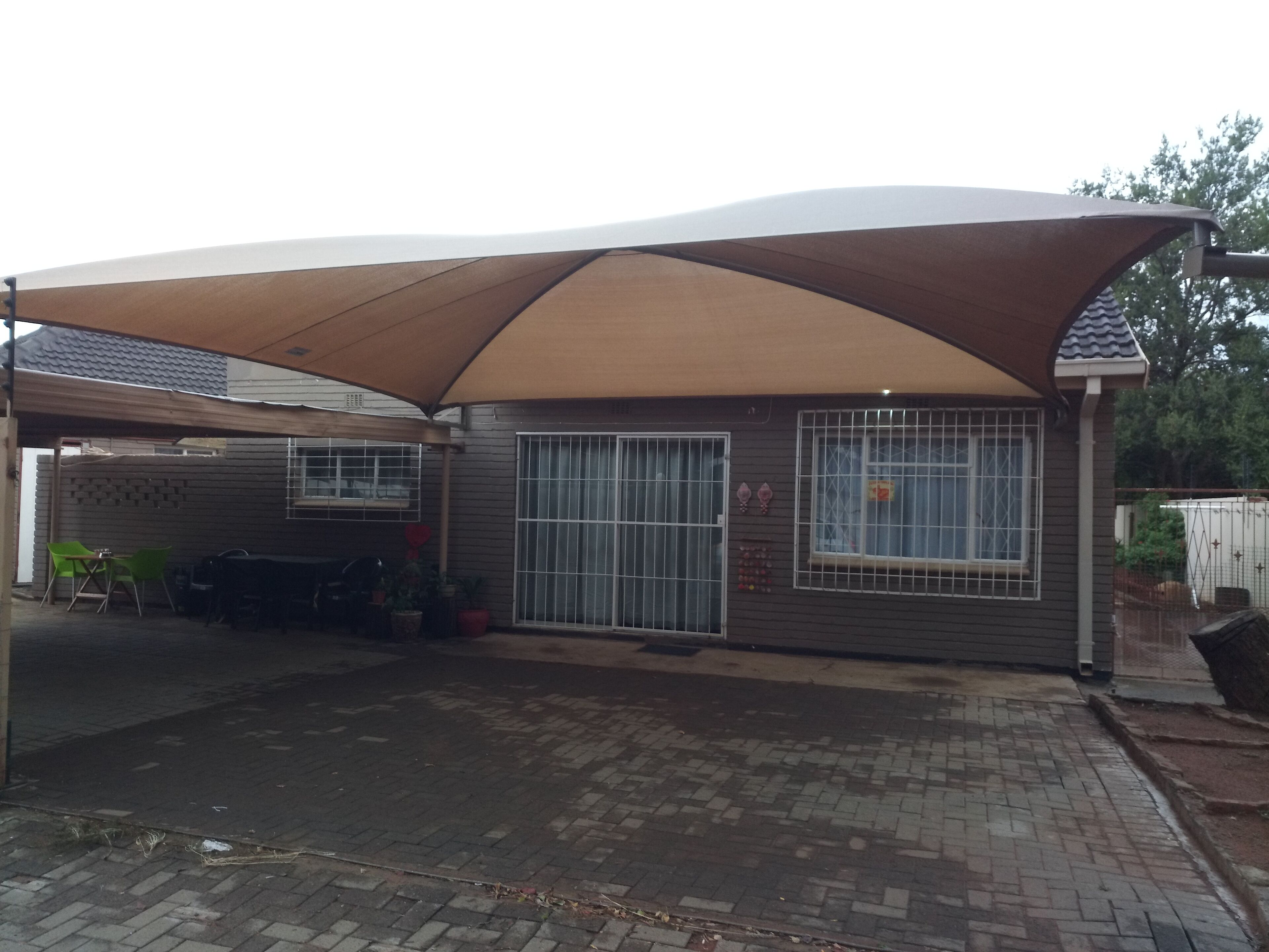 A covered outdoor area with a carport, a brick patio, and a building with barred windows and a door.