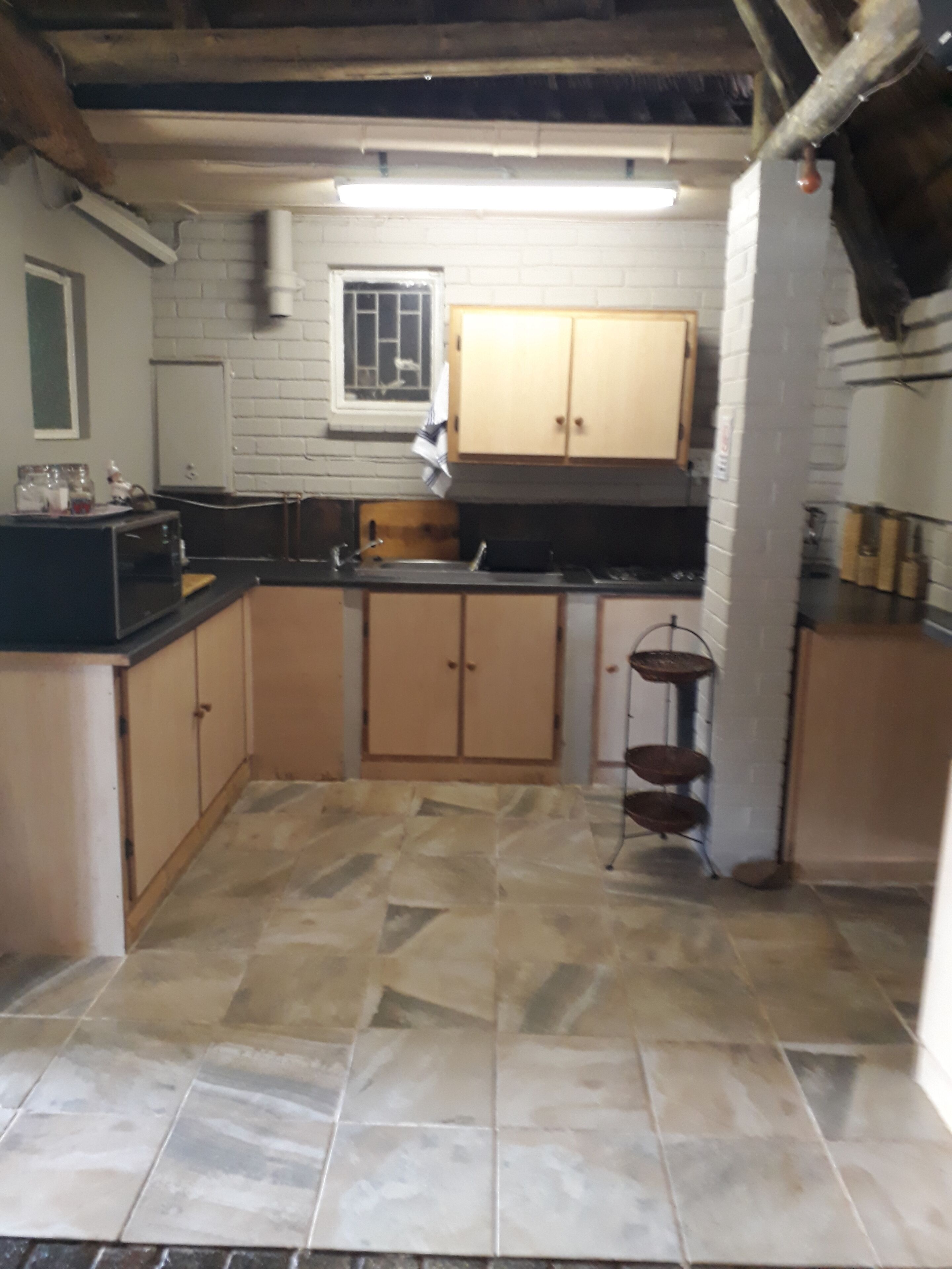 Una cocina con piso de baldosas, armarios de madera, un microondas y un lavamanos.